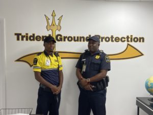 Two uniformed security guards standing confidently in front of Trident Ground Protection logo, representing licensed protection in South Florida.